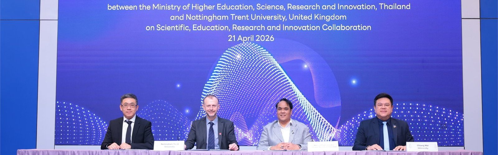 Four signatories seated at the MoU signing table, with the ceremony details and the date, 21 April 2026, on the screen behind them